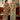 Two women in elegant sarees standing indoors with a painting in the background.