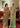 Two women in elegant sarees standing indoors with a painting in the background.